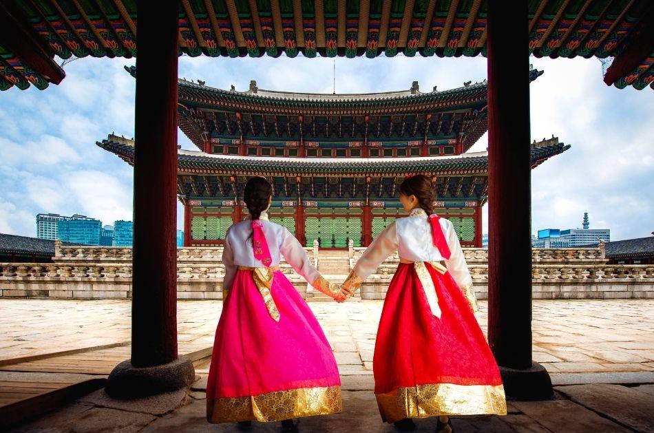 two korean girls dressed in hanbok holding hands in front of a palace in Seoul